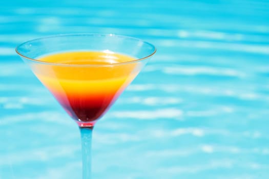 Colorful cocktail in front of attractive blue pool water