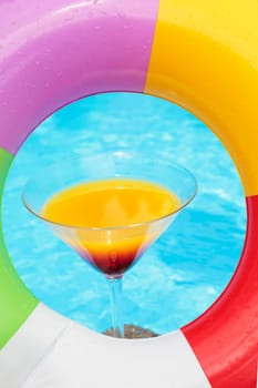 Colorful cocktail in front of attractive blue pool water seen through a rubber ring