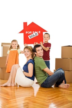 Happy family with cardboard boxes in their new home showing the house sold sign - isolated