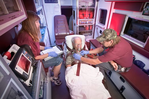 Two Emergency Medical Technicians treat an older patient inside the ambulance.