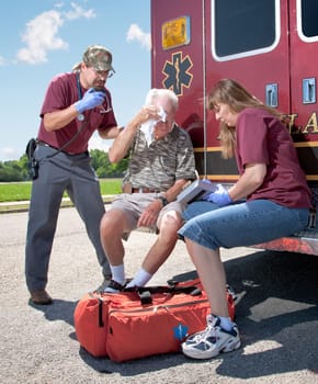 Two EMTs review a patients injuries while sitting on the back step of the ambulance