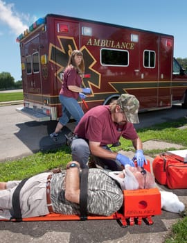 An EMT positions a patient with suspected neck / back injuries on a back board.  The patient is also wearing a cervical neck collar (C-collar).
