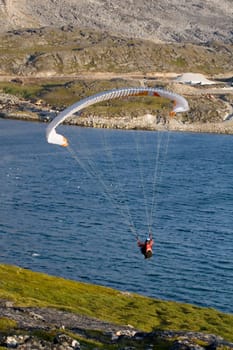 Paraglider hanging over the ocean. There is a mountain face in the background.