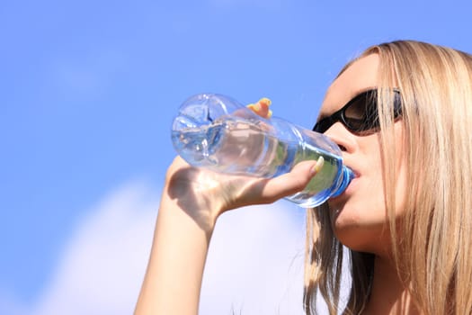 Girl drinking water against blue sky in sunny day