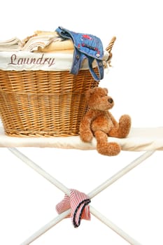 Teddy bear with laundry basket on ironing board against white background
