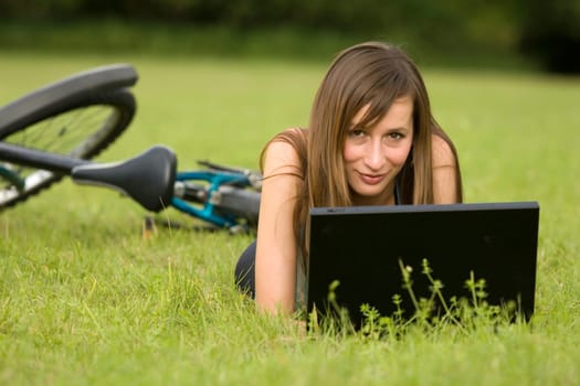 female student with laptop relaxing on the grass