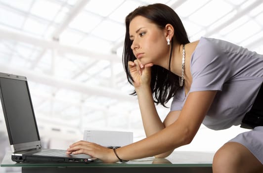 serious female is sitting on the desk, tipping on her laptop