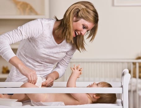 A young mother is changing her baby's diaper.  She is smiling and looking at her baby.  Horizontally framed shot.