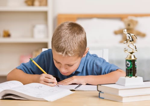A young boy is working on his homework at the table.  He is looking away from the camera.  Horizontally framed shot.