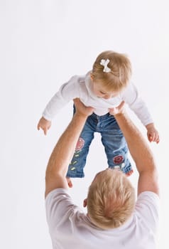 A father is holding up his daughter.  They are looking at each other.  Vertically framed shot.