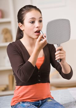 A young girl is looking into a hand mirror and putting makeup on.  Vertically framed shot.