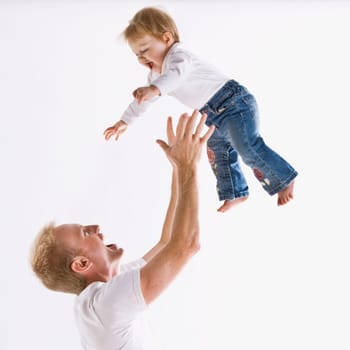 A young father is playing with his daughter and throwing her up in the air.  They are smiling at each other.  Square framed shot.