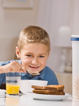 A young boy is eating breakfast and smiling at the camera.  Vertically framed shot.