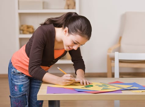 A young girl is working on a project.  She is smiling and looking down at her work.  Square framed shot.