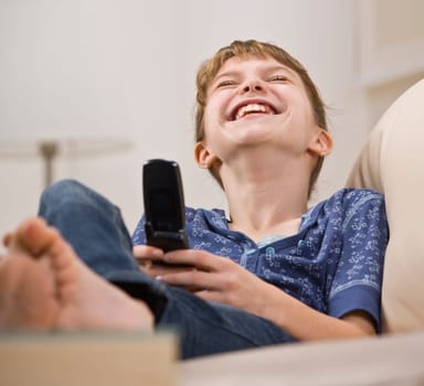 A young girl is holding a cell phone, looking away from the camera, and laughing.  Horizontally framed shot.