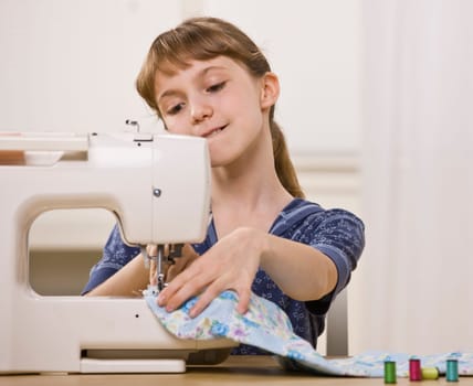 A young girl is sewing on a sewing machine.  She is looking away from the camera.  Horizontally framed shot.