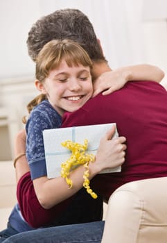 A young girl has received a gift from and is hugging her grandmother.  Vertically framed shot.
