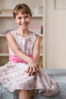 A young girl is seated inside and is smiling at the camera.  Vertically framed shot.