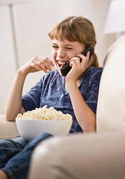 A young girl is sitting on the living room sofa and talking on a cell phone.  Vertically framed shot.