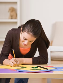 A young girl is working on a project.  She is smiling and looking down at her work.  Square framed shot.
