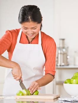 A woman is standing in a kitchen and slicing apples.  She is looking away from the camera.  Vertically framed shot.