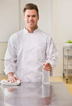 A young chef is cleaning the counter in a kitchen and smiling at the camera.  Vertically framed shot.