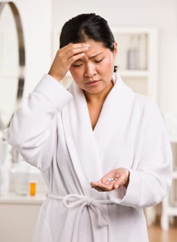 A young woman is holding pain medication that she is about to take for a headache.  She is looking away from the camera.  Vertically framed shot.