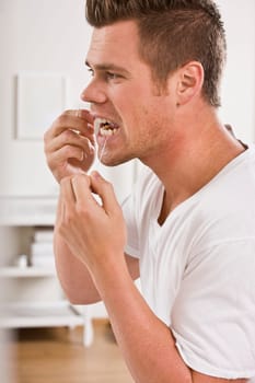 A man is standing in front of a mirror and flossing his teeth.  Vertically framed shot.