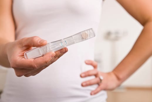 A woman is standing in her bathroom holding a pregnancy test in front of her.  Vertically framed shot.