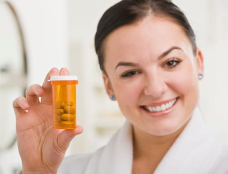 A woman is holding up a bottle of prescription medication and smiling at the camera.  Horizontally framed shot.