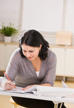 A young businesswoman is working on blueprints in an office.  She is looking away from the camera.  Vertically framed shot.