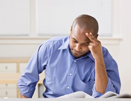 Attractive African American male sitting at desk looking at drawings. Horizontal