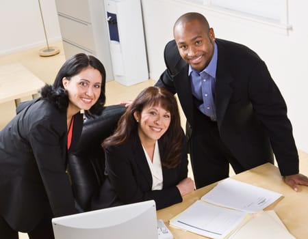 A group of business people are working together in an office.  They are smiling at the camera.  Horizontally framed shot.