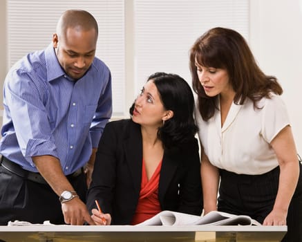 A group of business people are in an office and are looking at some paperwork.  They are talking and looking away from the camera.  Horizontally framed shot.