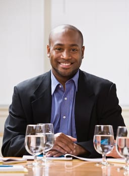 African American male sitting at desk with water, smiling at the camera. Vertical