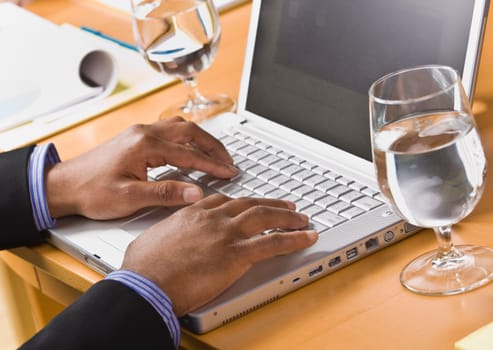 African American male hands typing on laptop keyboard. Glass of water on desk. Horizontal