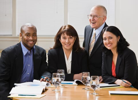 Four business workers, two men and two women, sitting at desk smiling at camera. Horizontal