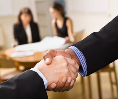 Mixed race handshake with two woman in background. Horizontal