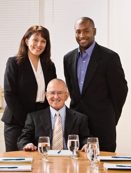 A group of business people are in an office and are smiling at the camera.  Vertically framed shot.