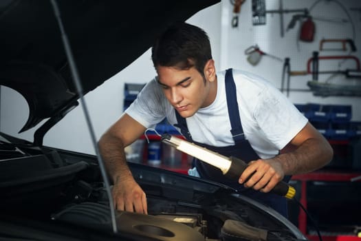 mechanic looking to car engine and holding lamp