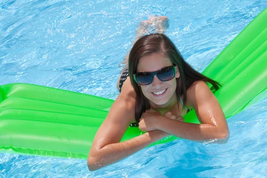 Attractive slim and tanned young lady lying on inflatable sunbed on sunny swimming pool on vacation or holiday