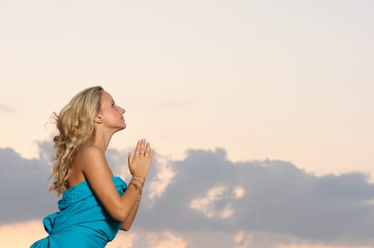 young blond girl praying outdoors at evening time