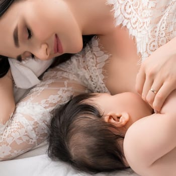 A mother bonds with her infant by breastfeeding while lying on a soft bed, creating a warm and intimate moment.