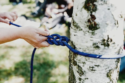 Women hands pull a strong blue rope tied to a birch tree. Professional zip line or cable car installation. Time for fun and relaxation. Family weekends activity together. High quality photo