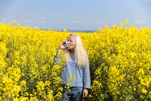 Elderly woman using an asthma metered dose inhaler in a blooming canola field