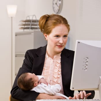 Businesswoman holding baby at desk
