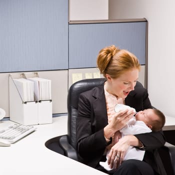 Businesswoman feeding baby at desk