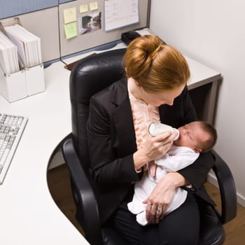 Businesswoman feeding baby at desk