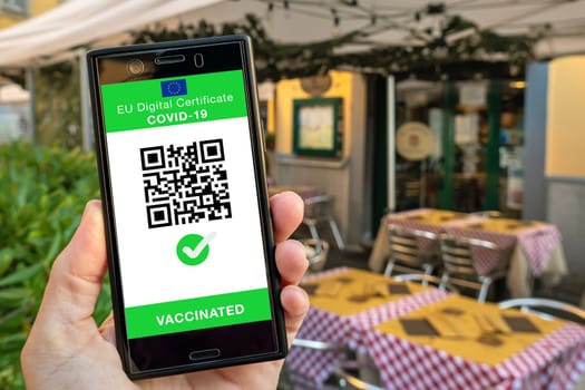 Woman showing on smartphone EU Digital Covid Certificate Green Pass with quad code. Restaurant background.