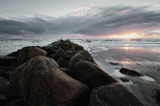 Sunset on the beach in Denmark. Stone groyne in the foreground. Walk on the coast in the sand. Landscape photo by the sea